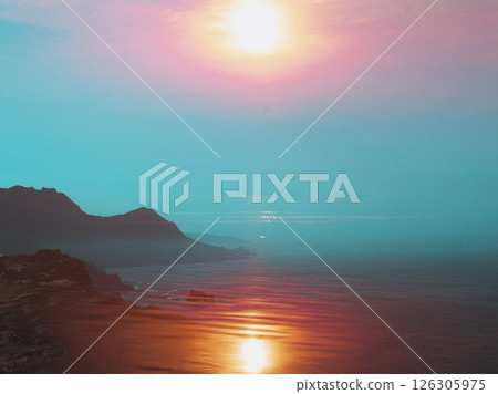 A stunning view of the ocean meeting the sky at sunset. The landscape reveals mountains. Nature's beauty reflected on the water creating magical scene 126305975