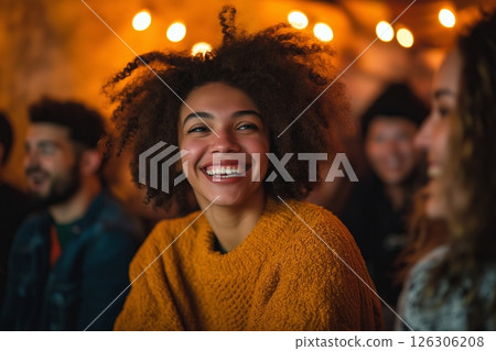 Smiling woman with natural hair and cozy sweater looks toward a friend in a warmly lit space 126306208