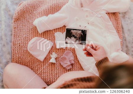 Expecting Mother Holding Ultrasound Image Next to Baby Clothes Expecting Mother Holding Ultrasound Image Next to Baby Clothes 126306240