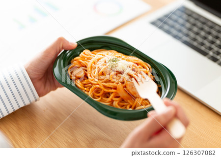 Middle-aged woman eating Neapolitan pasta at her desk in the office 126307082
