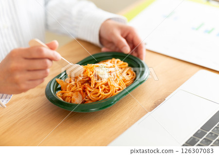 Middle-aged woman eating Neapolitan pasta at her desk in the office Middle-aged woman eating Neapolitan pasta at her desk in the office 126307083