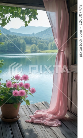 Pink curtain flows beside potted daisies on a wooden terrace overlooking a serene mountain lake 126307478