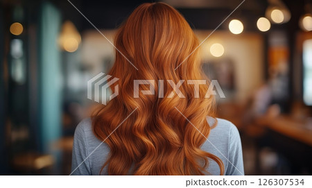 Glossy red waves falling down a back, lit by soft warm light in a warmly decorated indoor space 126307534