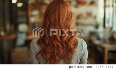 Long red hair with smooth waves flows naturally as the woman stands in a softly lit modern room 126307535