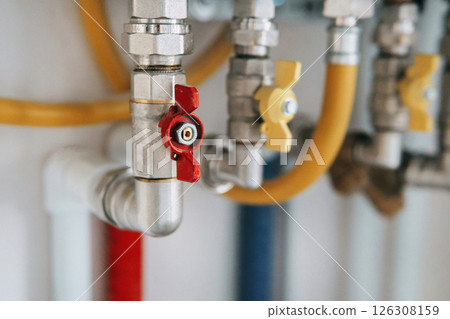Close-up view of water heater pipes and valves in a utility room, featuring colorful connectors and tubes. Essential components for heating system maintenance and operation. Gas boiler taps. 126308159