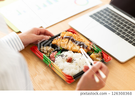 A middle-aged woman eating a tonkatsu bento at her office desk 126308368