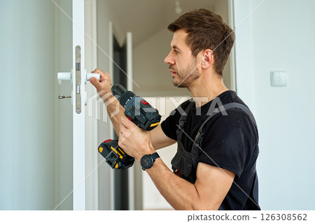 Man installs door in apartment during renovation, using cordless screwdriver Man installs door in apartment during renovation, using cordless screwdriver 126308562