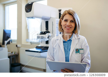 Smiling doctor standing next to mammogram machine in hospital Smiling doctor standing next to mammogram machine in hospital 126308809