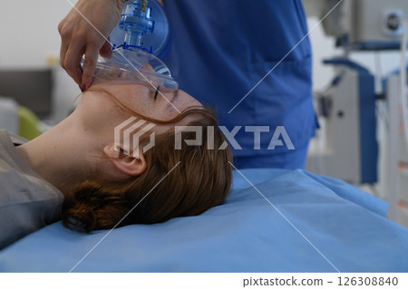 Medical staff applying oxygen mask to unconscious teenage girl in hospital. 126308840