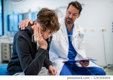 Depressed teenage patient sitting on hospital bed, talking with caring doctor. 126308904