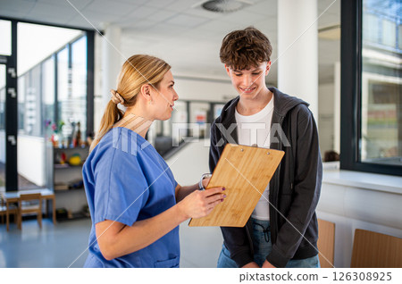 Doctor walking with teenage patient after successful medical procedure in hospital. 126308925