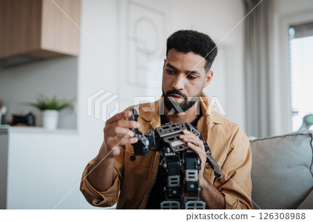 Handsome engineer student working on robot project at home. Handsome engineer student working on robot project at home. 126308988