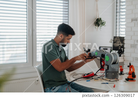 Young engineer building and programming a robotic arm at home. 126309017