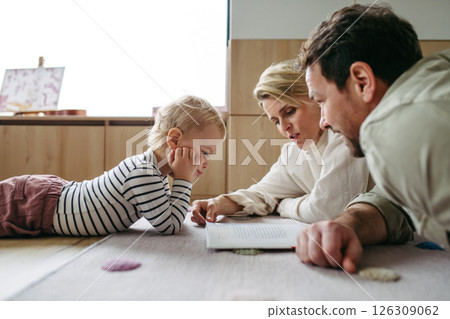 Parents reading book with little son, sitting on floor. 126309062