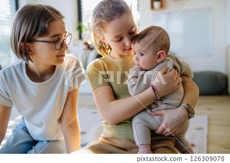 Big sisters holding small little brother in arms, taking care of him. Big sisters holding small little brother in arms, taking care of him. 126309078