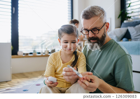 Diabetic girl taking blood sugar test at home, father helping her. 126309083