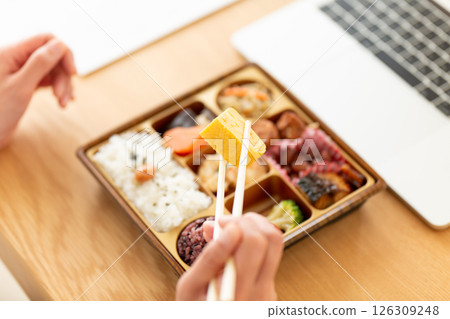 一位中年婦女在辦公室的辦公桌上吃日式便當 一位中年婦女在辦公室的辦公桌上吃日式便當 126309248
