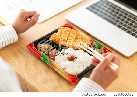 A middle-aged woman eating a tonkatsu bento at her office desk 126309332