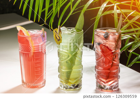 Colorful tropical cocktails with ice and fresh fruit garnishes on a sunlit table. lemonade, cold summer drink 126309559