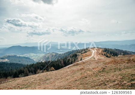 Winding mountain road stretching through scenic hills under a cloudy sky Winding mountain road stretching through scenic hills under a cloudy sky 126309563