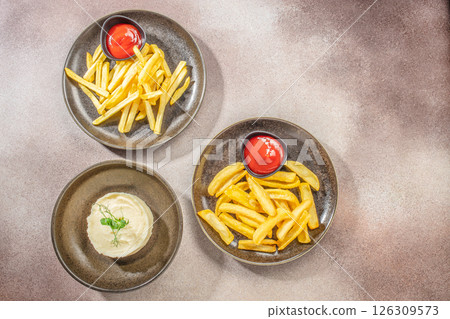 Plates of French fries with ketchup and mashed potatoes on a textured surface. top view. copy space for text 126309573