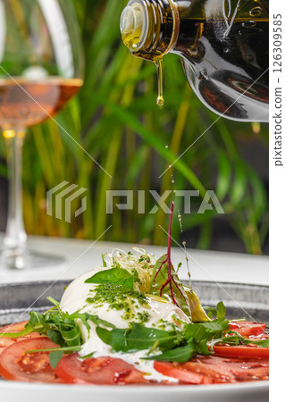 Drizzling olive oil over fresh burrata and tomato salad. delicious and healthy food for lunch or dinner 126309585