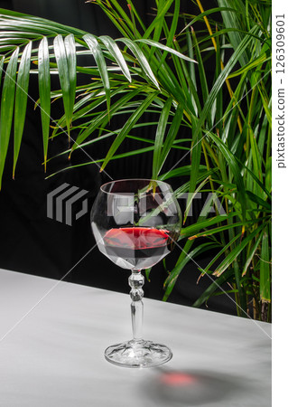 wine glass with red wine on table near green palm leaves 126309601