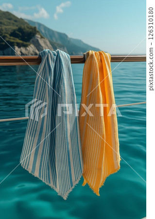 Two striped towels, one blue and one yellow, hang over a railing against the backdrop of the open sea. 126310180
