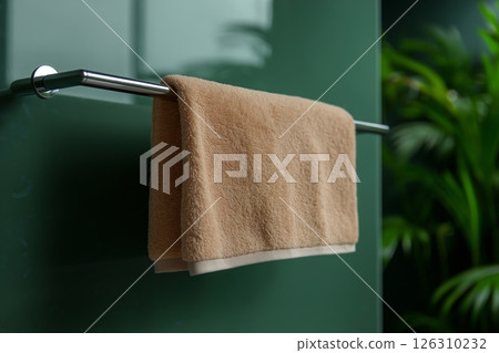 Beige towel hanging neatly on a silver rack, complemented by green foliage and soft natural light Beige towel hanging neatly on a silver rack, complemented by green foliage and soft natural light 126310232