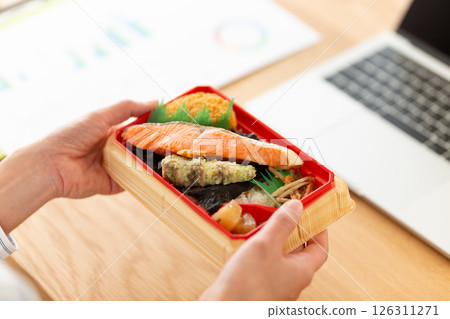 A middle-aged woman eating a salmon lunch box at her desk in the office 126311271