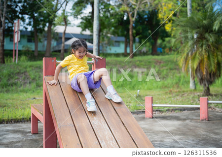 Asian Young child enjoying a sunny day at the playground, sliding down a wooden play structure, laughter and joy captured in outdoor playtime fun Asian Young child enjoying a sunny day at the playground, sliding down a wooden play structure, laughter and joy captured in outdoor playtime fun 126311536