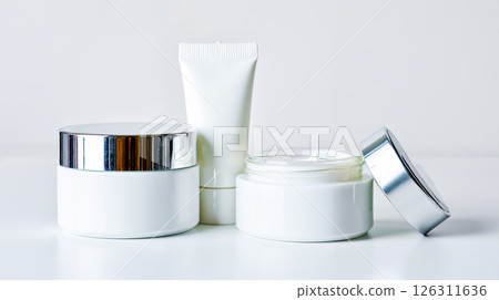 A white jar of cream next to a white container with a silver lid 126311636