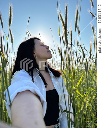 Woman Enjoying Sunlight in a Field of Tall Grass 126311842