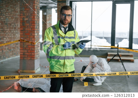 Man writing information into notepad. Detectives are collecting evidence in a crime scene near dead body Man writing information into notepad. Detectives are collecting evidence in a crime scene near dead body 126312013