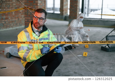 Sitting near caution police tape. Detectives are collecting evidence in a crime scene with dead body 126312025