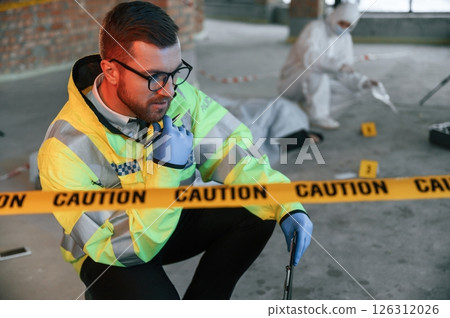 Sitting near caution police tape. Detectives are collecting evidence in a crime scene with dead body 126312026