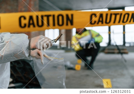 Woman holds the sleeve from the cartridge and puts it in the bag. Detectives are collecting evidence in a crime scene near dead body Woman holds the sleeve from the cartridge and puts it in the bag. Detectives are collecting evidence in a crime scene near dead body 126312031