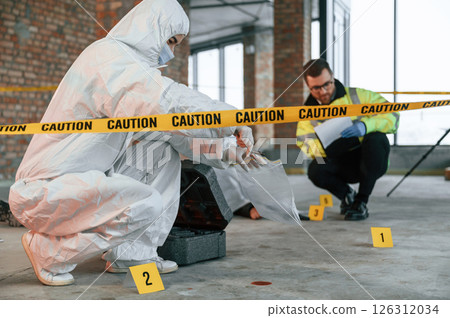Woman holds the sleeve from the cartridge and puts it in the bag. Detectives are collecting evidence in a crime scene near dead body 126312034
