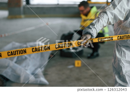 Close up view of caution police tape. Detectives are collecting evidence in a crime scene near dead body Close up view of caution police tape. Detectives are collecting evidence in a crime scene near dead body 126312043