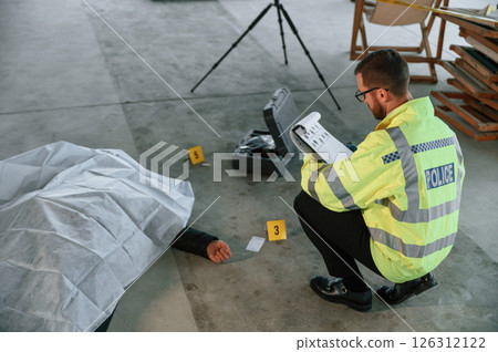 Notepad with information. Male detective is collecting evidence in a crime scene near dead body on the construction site 126312122