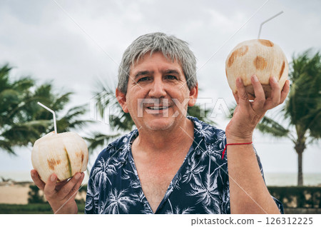 happy old male senior tourist holds a drinking coconut with a straw on vacation on beach by sea happy old male senior tourist holds a drinking coconut with a straw on vacation on beach by sea 126312225