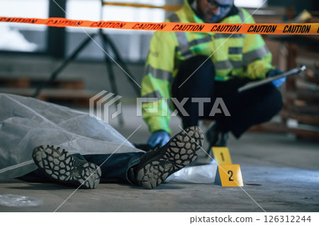 Male detective is collecting evidence in a crime scene near dead body on the construction site Male detective is collecting evidence in a crime scene near dead body on the construction site 126312244