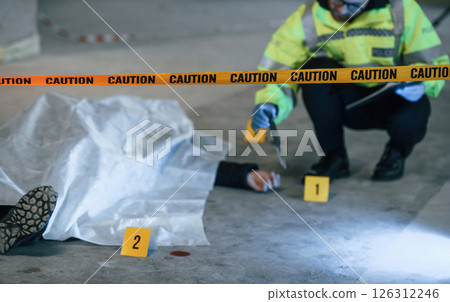 Knife is on the floor. Male detective is collecting evidence in a crime scene near dead body on the construction site 126312246