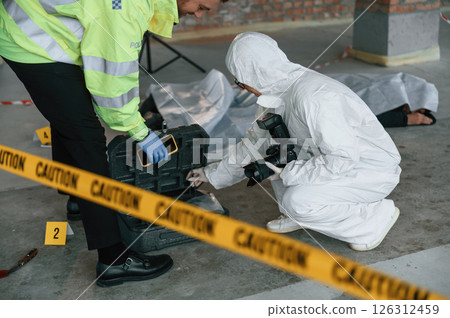 Caution police tape. Detectives are collecting evidence in a crime scene near dead body Caution police tape. Detectives are collecting evidence in a crime scene near dead body 126312459