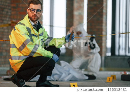Woman is using camera, making photos. Detectives are collecting evidence in a crime scene near dead body 126312481