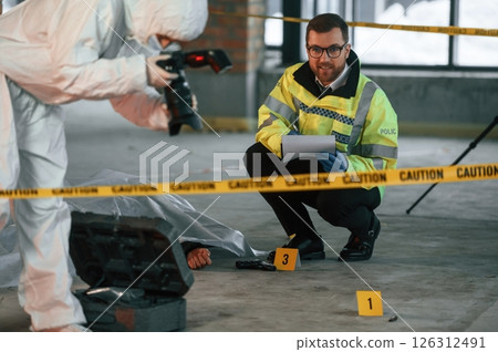 Woman is making photos by camera. Detectives are collecting evidence in a crime scene near dead body Woman is making photos by camera. Detectives are collecting evidence in a crime scene near dead body 126312491
