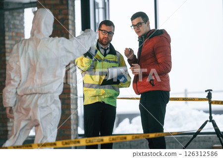 The witness is being questioned. Two detectives are collecting evidence in a crime scene The witness is being questioned. Two detectives are collecting evidence in a crime scene 126312586