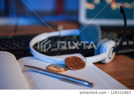Close up view of physical bitcoins, headphones, notepad and pen that is on the table Close up view of physical bitcoins, headphones, notepad and pen that is on the table 126312863