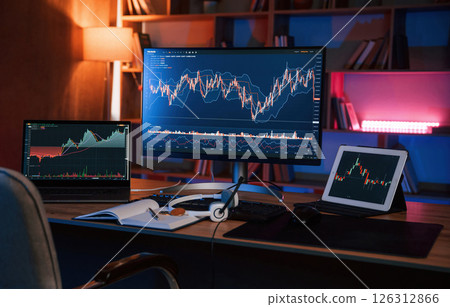 Computer with stock exchange graph on display is in the dark room with neon lighting Computer with stock exchange graph on display is in the dark room with neon lighting 126312866