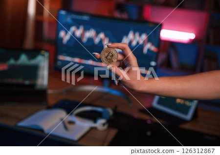 Close up view of woman's hand that holding bitcoin against computer display and tablet with graphs 126312867